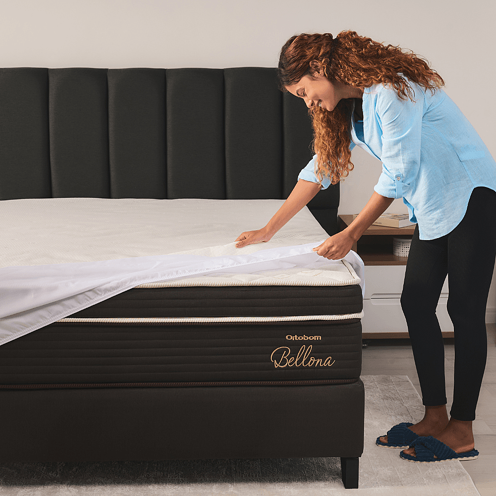 Colchão Ortobom Bellona — mulher ajustando protetor sobre colchão escuro